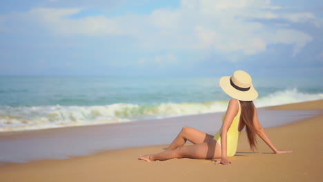 Lonely-Woman-in-Swimsuit-and-Summer-Hat-Sitting-on-Beach-Sand,-Looking-at-Waves-of-Tropical-Sea-on-Sunny-Day,-Slow-Motion