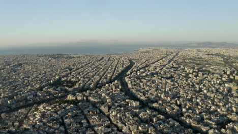 Drone-aerial-shot-over-the-city-of-Athens,-with-the-Mediterranean-Sea-in-the-background,-Greece