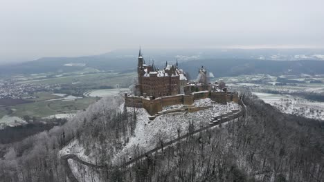 Aerial-flying-towards-medieval-Castle-Hohenzollern-on-a-mountain-on-a-snowy-day-during-winter-in-Swabia,-Germany