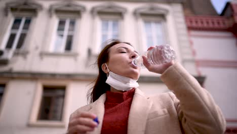 Beautiful-girl-wearing-protective-medical-mask-and-fashionable-clothes-drinks-water-with-bottle
