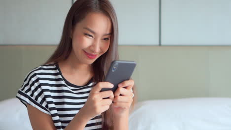 Pretty-young-lady-using-a-mobile-phone-holding-it-with-her-both-hands,-reading-a-message-and-smiling