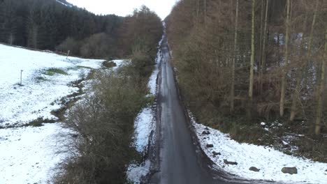 Snowy-Welsh-woodland-Moel-Famau-winter-landscape-aerial-dolly-right-view-across-road