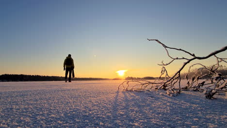 Lone-Male-winter-hiker-with-backpack-walks-across-frozen-lake-towards-golden-sunset