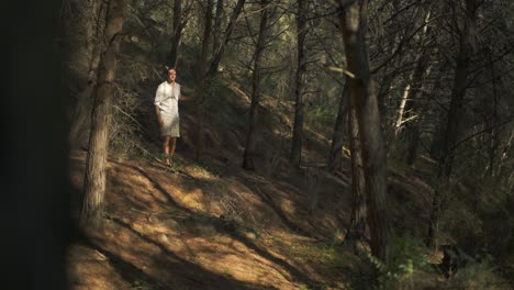 Young-hippie-nature-loving-man-walking-barefoot-through-forest-wearing-natural-clothing