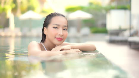 Porträt-Einer-Schönen-Asiatischen-Frau-Im-Poolwasser,-Die-In-Die-Kamera-Blickt