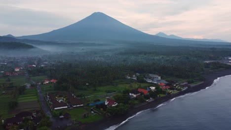 aerial-footage-amed-fisherman-village-at-sunrise-with-foggy-over-the-jungle-palm-tree-and-active-volcano-mount-Agung
