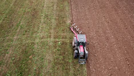 A-tractor-plowing-fields,-slow-aerial-pullback-from-close-to-wide