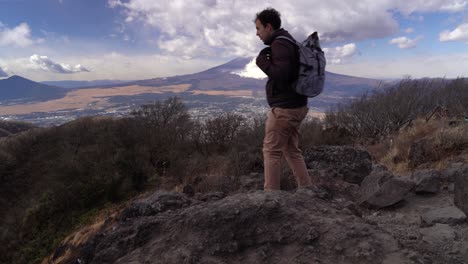 Excursionista-Masculino-Sentado-En-La-Cima-De-La-Montaña-Para-Descansar,-Monte-Fuji-En-Segundo-Plano.