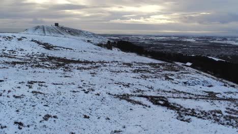 Snowy-Rivington-Pike-tower-Winter-hill-aerial-view-people-sledding-downhill-at-sunrise-orbit-right