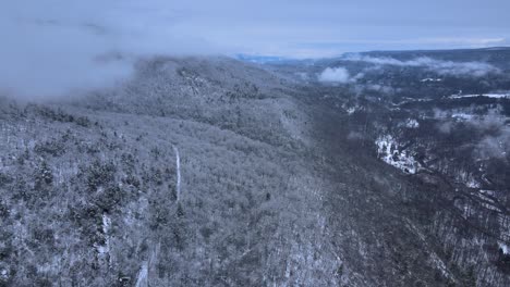 Volando-A-Través-De-Las-Nubes-Sobre-Montañas-Cubiertas-De-Nieve-Y-Bosques-En-Un-Hermoso-Valle-De-Montaña-Durante-El-Invierno-En-Un-Día-Nublado
