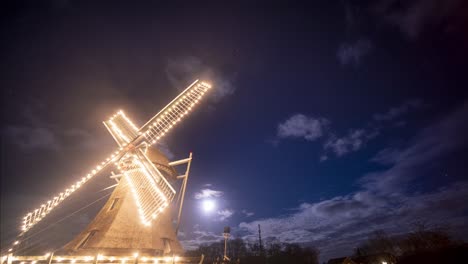 Brightly-illuminated-smock-mill-at-night-with-moving-clouds-in-background