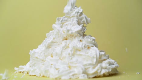 Whipped-cream-can-spraying-into-large-pile-panning-down-follow-slow-motion-with-yellow-studio-backdrop
