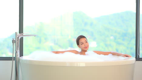 A-pretty-young-woman-daydreams-as-she-takes-a-soothing-bubble-bath-backed-by-a-spectacular-view