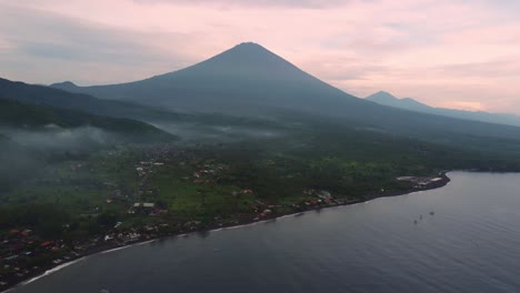 Vista-Aérea-Amed-Bali-Indonesia-Pequeño-Pueblo-De-Pescadores-En-El-Océano-Con-Volcán-De-Monte-Activo-Durante-La-Colorida-Puesta-De-Sol