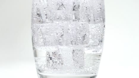 Soda-Oder-Sprudelndes-Wasser,-Das-Auf-Eiswürfel-Gießt,-Die-Glas-In-Zeitlupenblasen-Füllen,-Nahaufnahme,-Weißer-Studiohintergrund-Der-Karbonisierung
