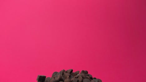 Schokoladenstückchen,-Die-In-Zeitlupe-Auf-Den-Haufen-Fallen,-Mit-Rosa-Hintergrund,-Nahaufnahme-Makro