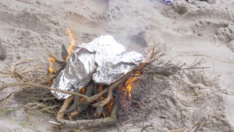 Fish-wrapped-in-foil-cooking-on-a-fire-on-the-beach