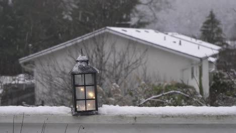Electric-lantern-sitting-on-top-of-a-deck-railing-during-a-light-snowfall