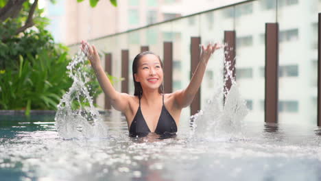 Close-up-of-a-very-happy-and-playful,-young-woman-splashing-water-while-in-the-hotel-pool