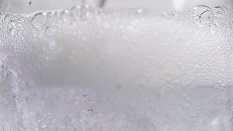 Soda-Auf-Eiswürfel-Im-Glas-Gießen-Makro-Mit-Kohlensäure-Auffüllen-Blasen-In-Zeitlupe-Sprudelwasser-Nahaufnahme-Gießen