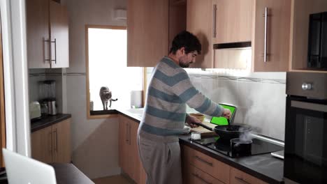 Vista-Principal-De-Un-Hombre-Con-Camiseta-Despojada-Usando-Una-Tableta-Para-Cocinar-En-La-Cocina-Mientras-Sigue-Una-Receta-De-Internet