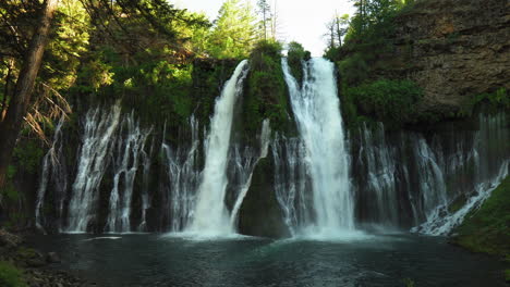 Panning-shot-of-Burney-Falls,-forest-waterfall-in-California,-with-water-falling-down-a-cliff