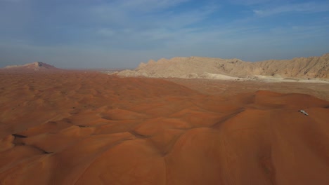Wüste-Der-Vereinigten-Arabischen-Emirate:-Blick-Von-Oben-Auf-Die-Wüste-Von-Sharjah,-Eine-Gruppe-Von-4x4-Fahrzeugen,-Fahrten-Auf-Riesigen-Sanddünen,-Mleiha-Berge-Im-Hintergrund