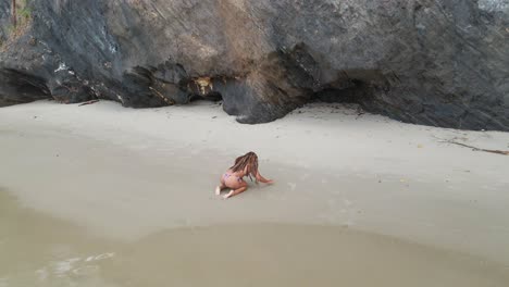Ein-Bikini-Mädchen,-Das-Sich-Am-Strand-Mit-Felsigen-Klippen-Im-Hintergrund-Amüsiert