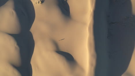 Filmische-Aufsteigende-Drohnenaufnahme-Eines-Mannes,-Der-Allein-Auf-Sanddünen-Oder-In-Der-Wüste-Läuft