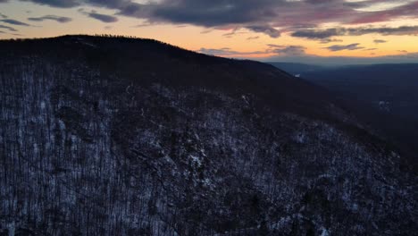 Drone-footage-of-a-forested-mountain-covered-in-light-snow-during-winter-at-dusk-in-the-Appalachian-mountains