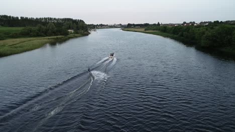 Tracking-Aerial-View-of-Man-Water-Skier-and-Tow-Boat-in-a-Calm-River-Bann-Water,-Coleraine,-Northern-Ireland,-Great-Britain,-60fps-Drone-Shot
