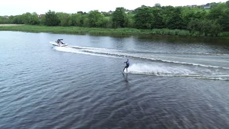 Waterskiing-in-River-Bann,-Northern-Ireland-UK,-Slow-Motion-Aerial-View-of-Skier-and-Tow-Boat,-Tracking-Drone-Shot