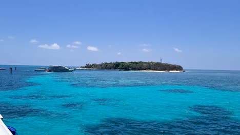 View-Going-Past-Boat-Docked-At-Pier-On-Green-Island-Surrounded-By-Turquoise-Waters