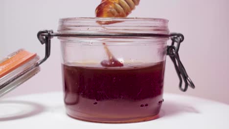 Honey-utensil-dips-in-dark-honey,-drizzles,-then-sinks-in-glass-jar,-Closeup