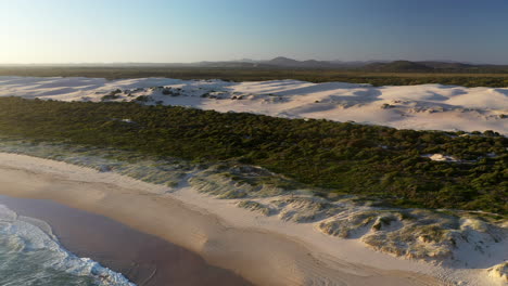Cinematic-wide-drone-shot-of-the-Dark-Point-sand-dunes-revealing-the-beach-and-ocean-at-Hawks-Nest,-New-South-Wales,-Australia