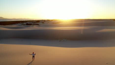 Epic-drone-shot-into-the-sun-of-a-silhouetted-man-walking-on-sand-dune