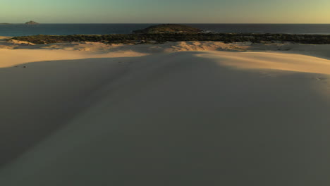 Drone-shot-of-man-running-on-top-of-sand-dune-at-the-Dark-Point-sand-dunes-at-Hawks-Nest,-New-South-Wales,-Australia