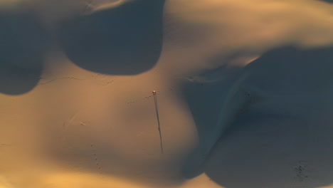 Cinematic-rising-drone-shot-of-man-walking-alone-on-sand-dunes-or-the-desert