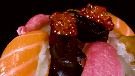 Makroansicht,-Die-Sich-über-Eine-Rotierende-Nigiri-Sushi-Auswahl-Auf-Schwarzem,-Reflektierendem-Glashintergrund,-Toro-Thunfisch,-Lachs,-Zitronenfisch,-Lachsrogen-Und-BBQ-Aal-Bewegt