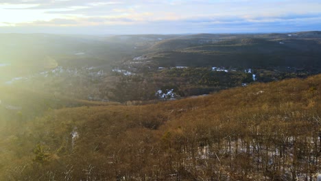 Aerial-footage-of-a-forested-mountain-valley-with-a-light-coating-of-snow-during-winter-in-the-Appalachian-Mountains-during-sunset’s-golden-hour-in-winter