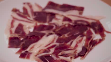 Hand-holding-slice-of-Jamon-Iberico-close-up-and-setting-down-on-plate