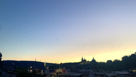Weite-Sicht-Auf-Die-Vögel,-Die-In-Der-Abenddämmerung-über-Die-Prager-Burg-Und-Die-Skyline-Fliegen