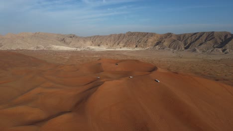 UAE-Desert:-Top-View-of-Sharjah-Desert,-A-group-of-4x4-vehicles,-rides-on-Giant-Sand-Dunes,-Mleiha-Mountains-in-the-Background