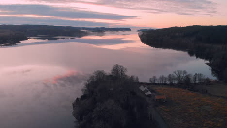 Aerial-view-of-a-pink-sunset-sky-reflecting-into-a-calm-lake,-wide-shot,-drone-flying-forward