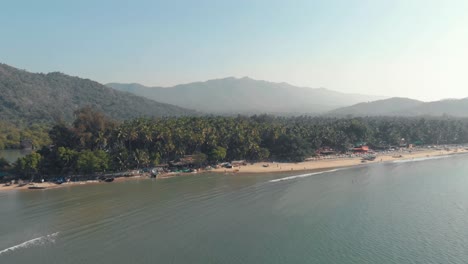 Coastal-exotic-shoreline-and-tourist-beach-resort-in-Palolem-Beach,-in-Goa,-India---Aerial-wide-slide-shot
