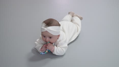 Newborn-In-White-Jumpsuit-Match-To-Her-Headband-Lying-On-Her-Stomach-While-Playing