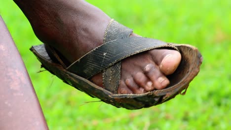 Closeup-of-a-man-tapping-with-his-Masai-footwear,-while-sitting-in-African-Jungle
