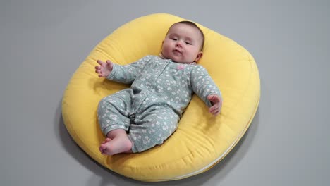 Smiling-Baby-Lying-On-His-Back-On-A-Yellow-Comfy-Round-Cushion---High-Angle-Shot