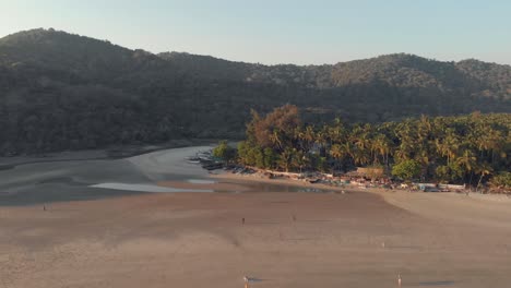 4k-aerial-drone-footage-of-a-beach,-at-sunset,-during-a-low-tide-at-the-tourist-destination-spot-of-Palolem,-India