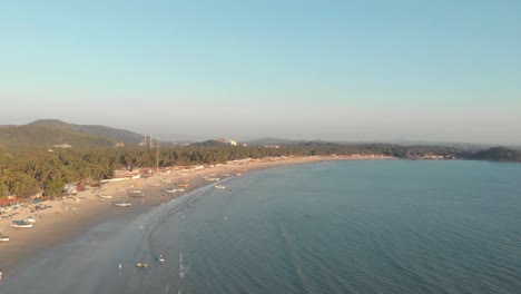 Coastline-stretching-across-the-horizon-with-fishing-boats-moored-on-the-golden-sands-near-the-coast-in-Palolem-Beach,-in-Goa,-India---Aerial-Panoramic-shot